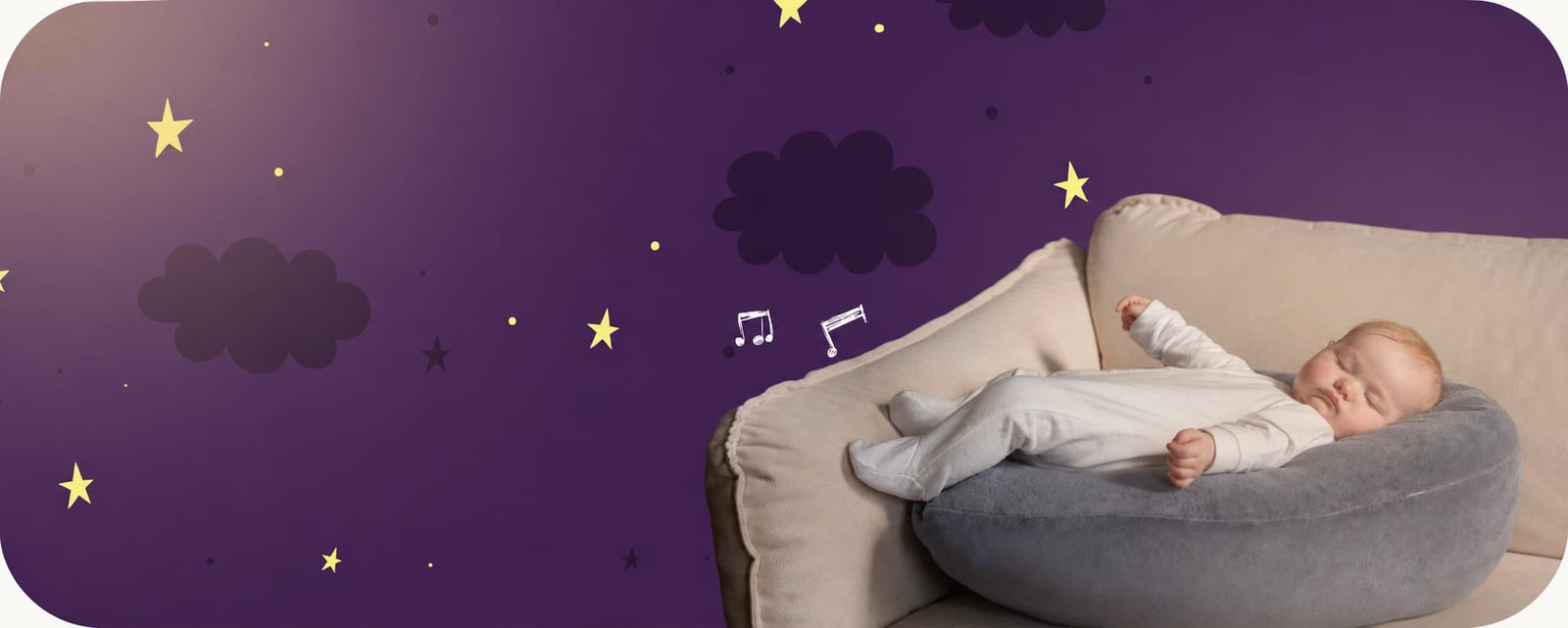 A sleeping baby wearing a white onesie rests on a gray crescent-shaped baby pillow on a beige sofa, set against a purple wall decorated with stars and clouds.