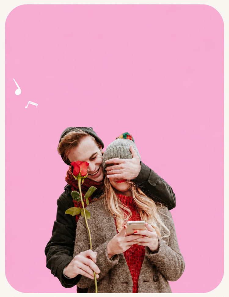 Romantic personalized wedding song banner featuring a smiling couple in winter clothing, with the man covering the woman’s eyes and holding a red rose, set against a pink rounded background with white music notes and open space for website text.